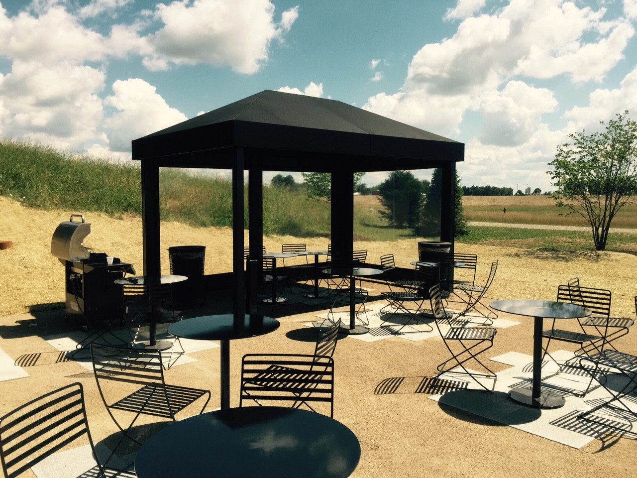 A black gazebo with tables and chairs around it.