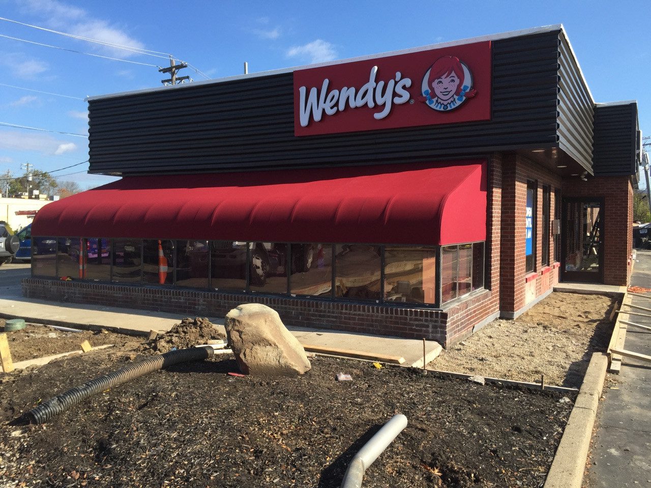 A wendy 's restaurant with a red awning and dirt.