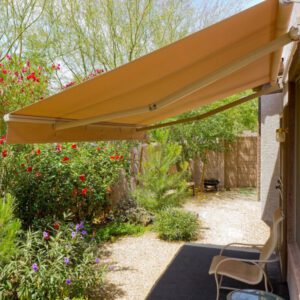 A patio with an awning and chair in the middle of a garden.